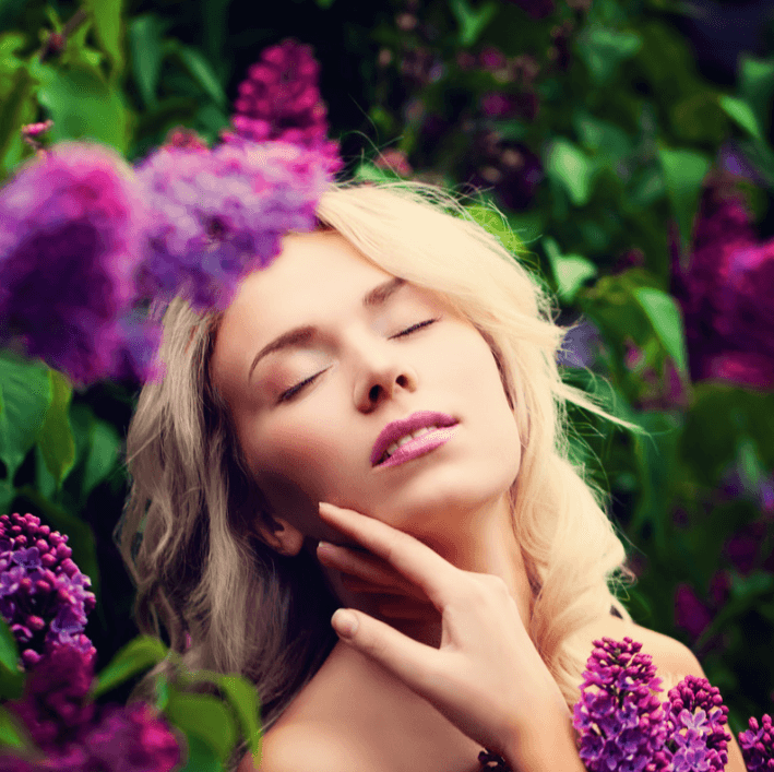 A serene woman enjoying the scent of lilacs, representing natural beauty and skincare with Smoother Oil.