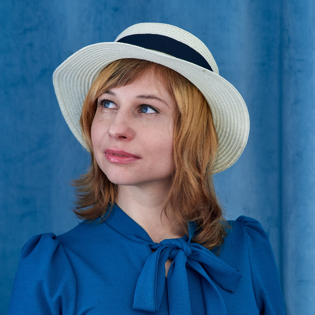 Woman wearing a straw hat and a blue blouse, looking thoughtfully to the side with soft-focus background.